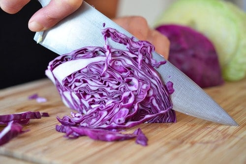 Someone thinly slicing red cabbage on a cutting board for sautéed red cabbage with onions, garlic, and anchovy.