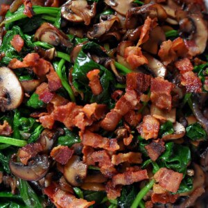 An overhead shot of a plate filled with sautéed spinach, crispy bacon bits, shallots, and mushrooms.