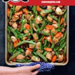 An overhead shot of sheet pan chicken stir-fry fresh out of the oven. A hand is holding the edge of the pan with a towel. The red banner at the bottom reads paleo, Whole30, gluten-free.