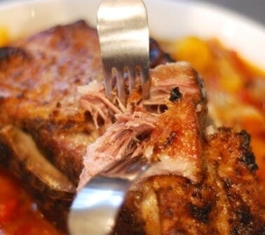 A bowl of slow cooker pork pot roast in a bowl with someone shredding the meat with two forks.
