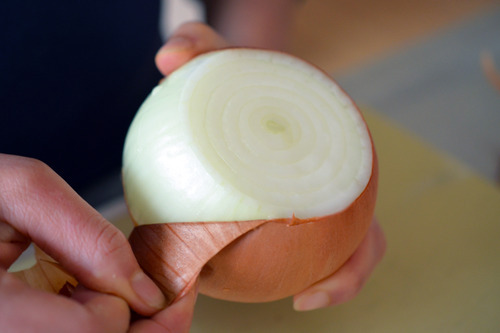 Someone peeling the outside skin of a yellow onion.