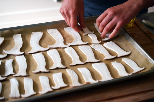 Someone lining thinly sliced mushrooms in rows on a baking tray to make crispy mushroom chips.