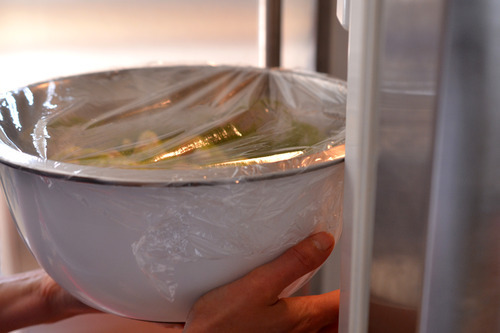 Someone putting a bowl of marinated chili lime chicken in the fridge.