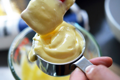Someone spooning the mayonnaise mixture of smoked paprika and tabasco into a measuring cup.