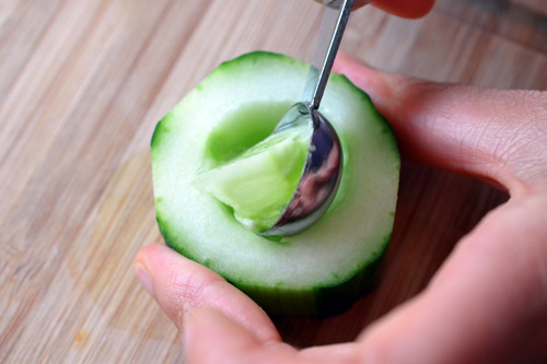 Someone scooping out the inner seeds of the chopped cucumbers.