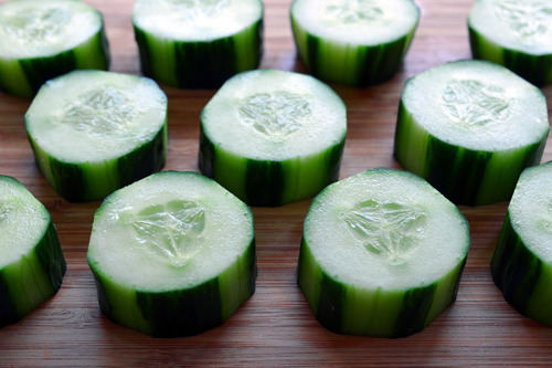 Sliced cucumbers sitting on a cutting board neatly in rows.
