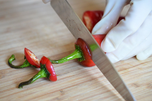Cutting the stems off red jalapeño peppers while wearing latex gloves