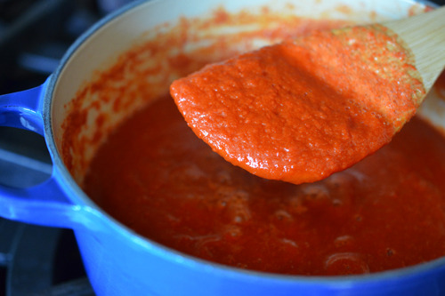 A shot of a wooden spatula spooning out Whole30® Sriracha from a enameled cast iron sauce pan.