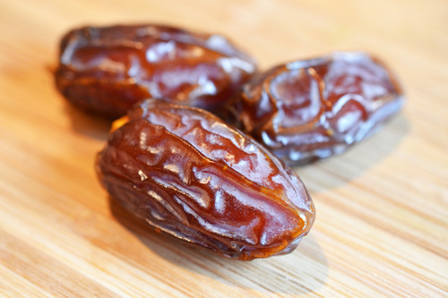 A closeup of three dried Medjool dates on a wooden cutting board.