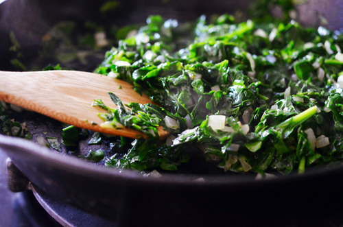 Sautéeing spinach and onions in a skillet.