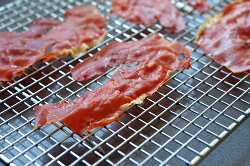 Slices of prosciutto on a wire rack ready to be baked.
