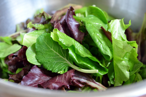 Mixed greens in a metal bowl for fig and watermelon salad.