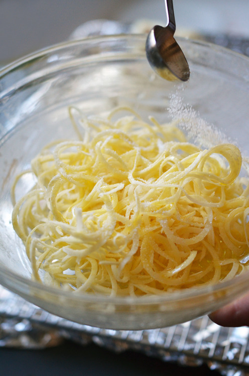 Sprinkling salt on spiraled white sweet potatoes to make healthy Yummy Mummies for Halloween