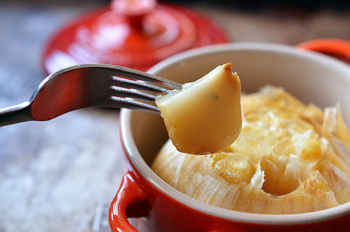 A fork taking our a single garlic bulb from a roasted garlic head.