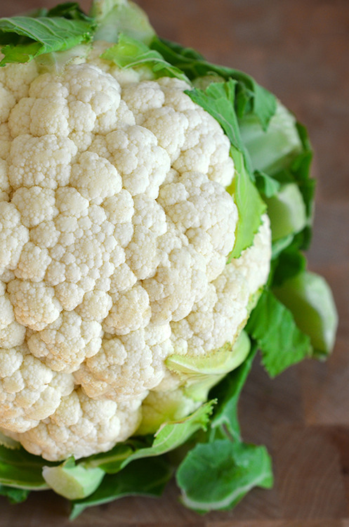 A whole raw cauliflower sitting on a cutting board.