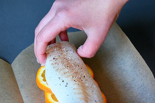 Laying the seasoned cod fillet on top of the orange slices.