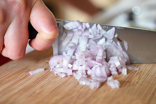 A closeup of mincing a shallot on a wooden cutting board with a chef's knife.