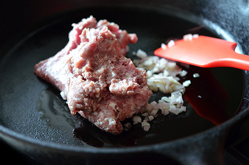 A cast iron skillet contains ground pork and shallots. 