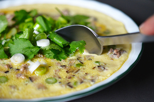 Someone using a spoon to scoop out Cantonese Egg Custard with Minced Pork 