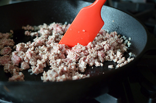 A cast iron skillet with the cooked pork and shallots.