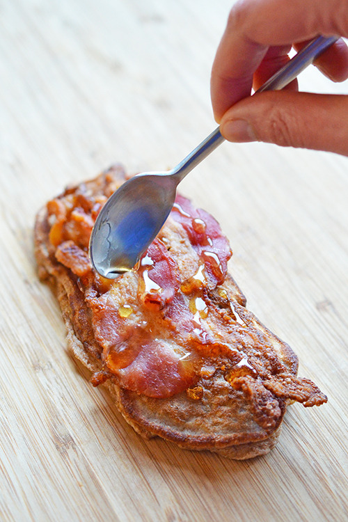 Maple syrup is being spooned on an open-faced Bacon Pancake Sandwich.