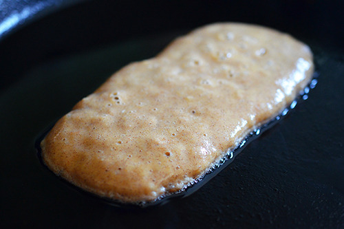 A rectangular shaped paleo pancake is frying in a cast iron skillet. 