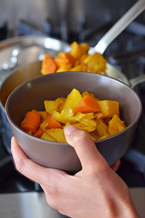 Spooning paleo Atkilt (Spiced Ethiopian Vegetable Stew), a tasty blend of cabbage, carrots, and potatoes into a bowl.