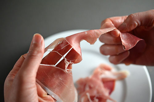 Two hands tearing up a piece of prosciutto for Pig In A Skillet.