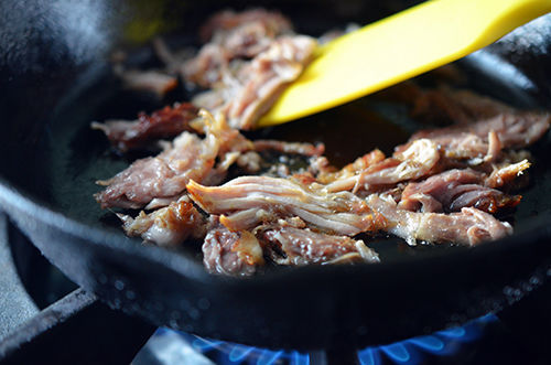 Leftover kalua pig being fried crispy in a small cast iron skillet.