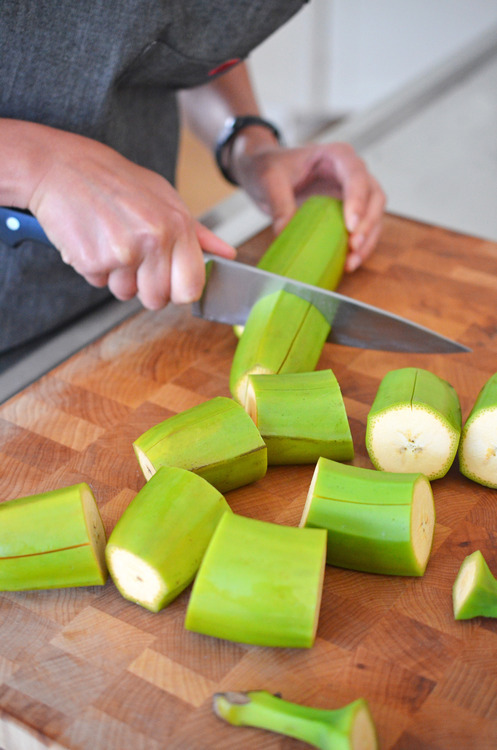 Someone cutting up green plantains into large chunks.