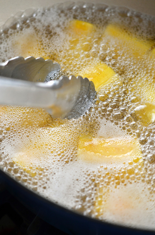 Pieces of green plantain frying in a pot filled with oil.