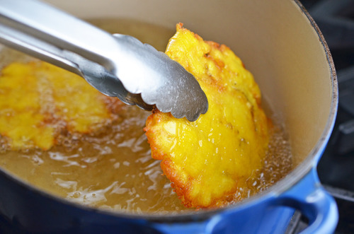 A silver tong taking a fried patacone out of the oil.