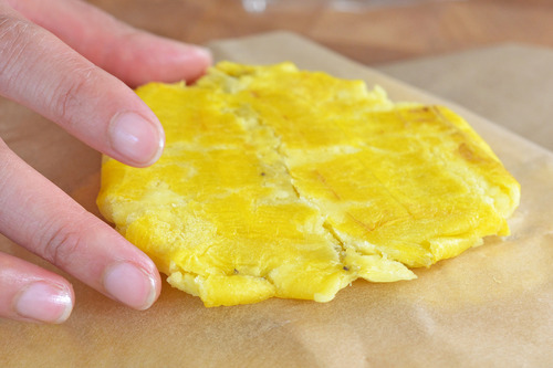 A close up of a smashed fried green plantain with someone holding it at the edges.
