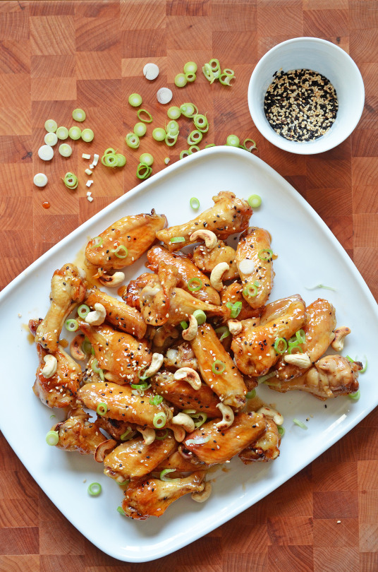 Sticky sesame teriyaki chicken wings piled on a plate on a wood cutting board.