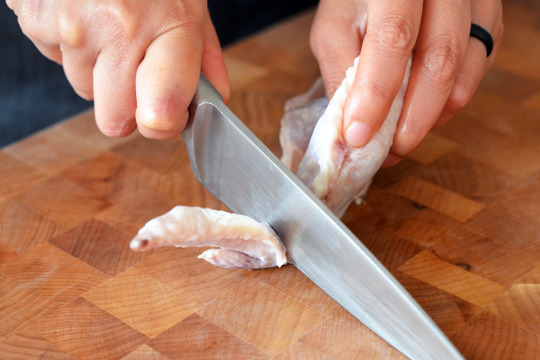 Someone cutting the joint in between the chicken wing in between the wing and drumette.
