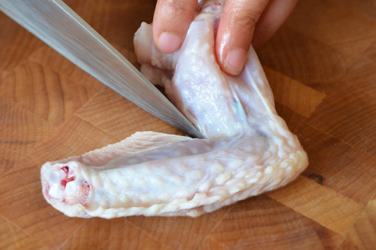 Someone making a small incision on a chicken wing in between the wing and drumette.