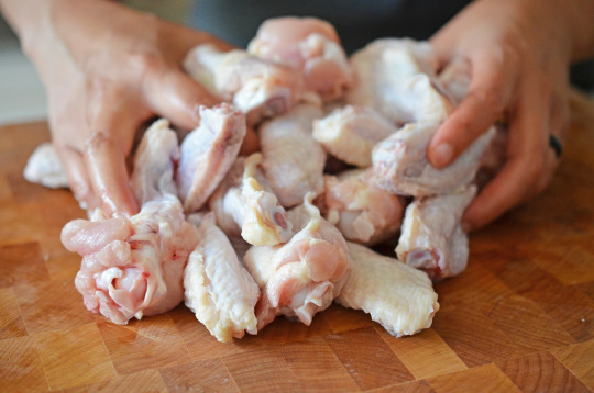 Someone putting raw chicken wings on a wood cutting board.