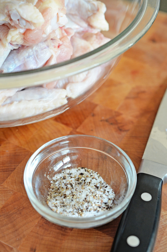 Raw chicken wings in a bowl with a small bowl of seasoning to the side.