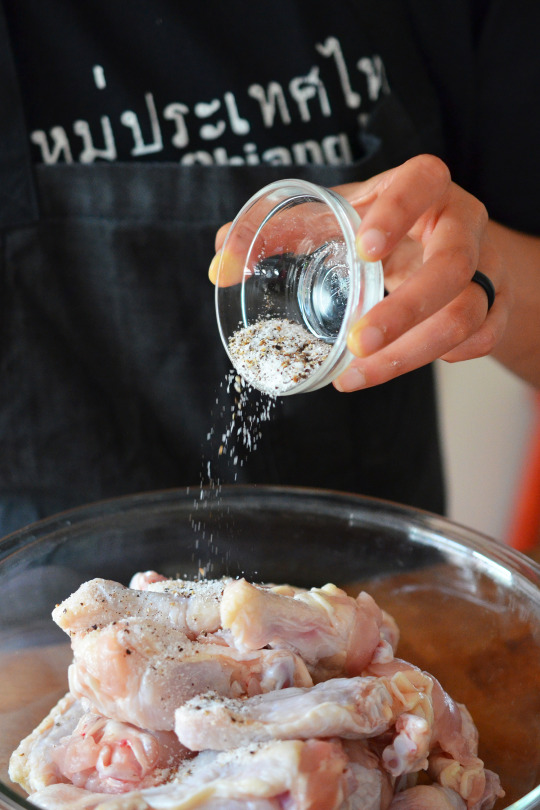 Adding salt and pepper to a bowl of raw chicken wings.