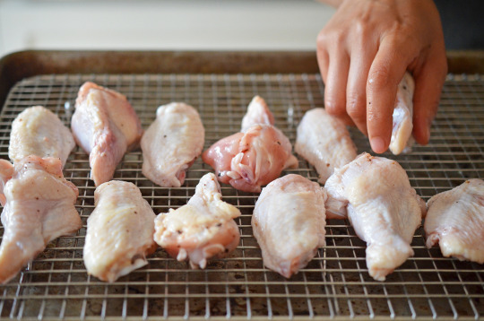 Someone putting raw chicken wings on a wire rack.