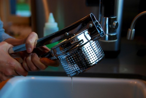 Someone squeezing a potato ricer full of collard greens to drain the water.