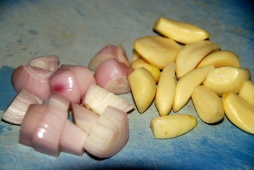 Coarsely chopped onions and garlic cloves on a cutting board.