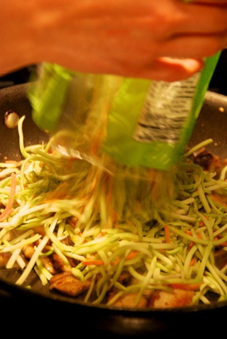Someone adding a bag of broccoli slaw to a pan.