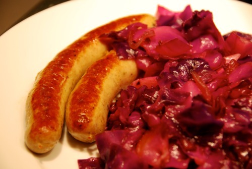Paleo and Whole30 sautéed red cabbage with onions, garlic, and anchovy on a plate with brats.