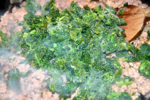 Frozen spinach in a cast iron skillet with ground pork.