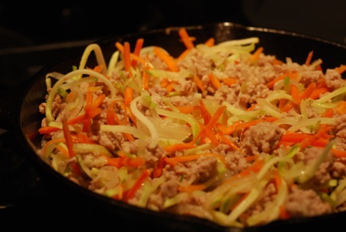 Broccoli slaw frying in a cast iron skillet with ground pork and onions.