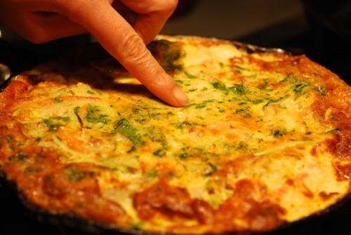 Someone poking the top of a frittata to check its doneness.