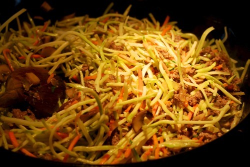 A mix of broccoli slaw being sautéed with ground beef, onions, and cremini mushrooms.