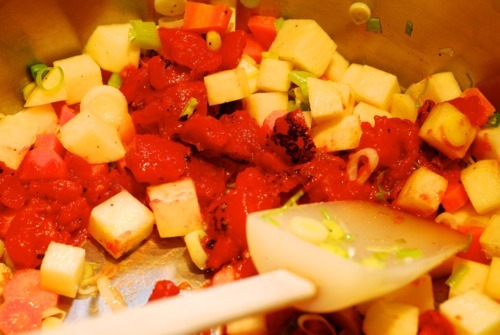 Fire roasted tomatoes are added to the pan that already has turnips, carrots, green onions, and garlic.