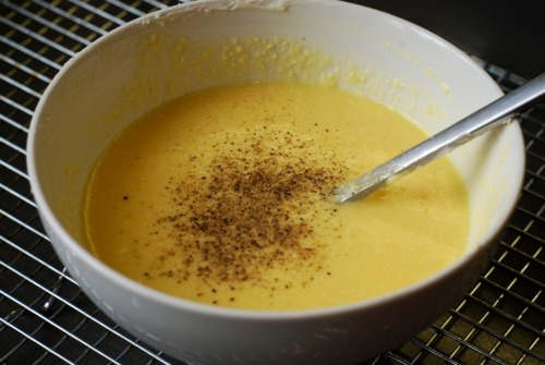 A bowl of whisked eggs with yogurt, cheese, salt, and pepper with a spoon inside.